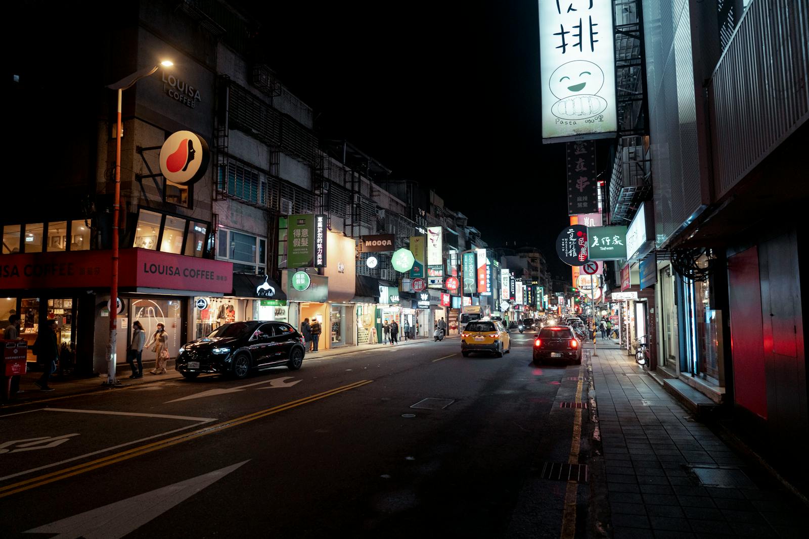 Bustling night street in Taipei with bright city lights and urban activity.